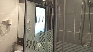 Ett modernt badrum med en dusch som är avskärmad med glasväggar, en hårtork och en toalett.