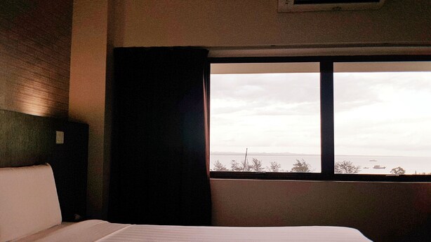 Ett hotellrum med en stor säng, ett fönster med utsikt över havet och en luftkonditioneringsanläggning på väggen.