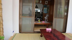 Ein traditioneller japanischer Raum mit Tatami-Boden, einer Schiebetür, einem Holztisch und einem Fächer.