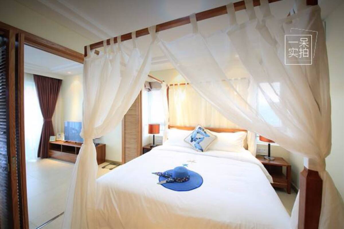 Habitación de hotel con cama cubierta por un dosel, una mesita de noche con lámpara y vista al interior de la habitación.