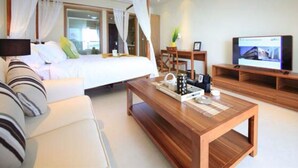 Quarto de hotel moderno com cama, mesa de centro de madeira, televisão e área de estar com sofá e poltronas.