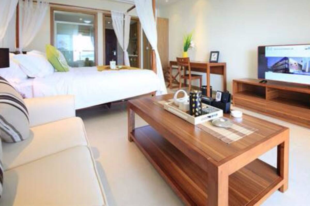 Una habitación de hotel moderna con cama, una mesita de centro de madera, televisor y una zona de estar con sofá y sillones.