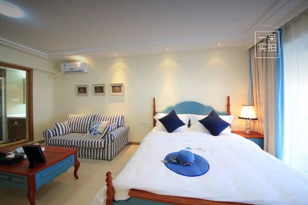Una habitación de hotel con cama, un sofá a rayas, una mesita de noche de madera con lámpara y un espejo en la pared.
