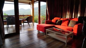 Una sala de estar moderna con un sofá rojo, una mesa de centro de vidrio y vistas a un paisaje montañoso a través de amplios ventanales.