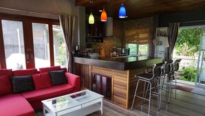 Un espacio moderno para el estar con un sofá rojo, una mesa de centro blanca, una cocina con salpicadero de piedra y una zona de bar con taburetes.