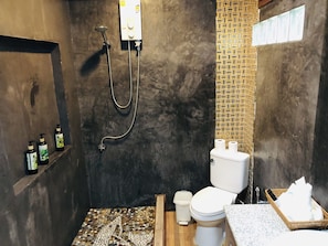 A compact bathroom with a shower, toilet, and a small shelf with toiletries.