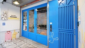 Una puerta azul con cerradura de seguridad y mirilla, un letrero con ilustración de conejo, y un piso de baldosas.