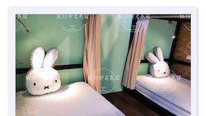 Una habitación de hotel con cama, almohada con diseño de conejo y espejo que refleja la habitación.