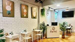 Una cafetería con paredes de ladrillo blanco, una recepción y varias mesas con sillas.