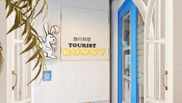 Un pasillo con una puerta blanca, un ventanal con marco azul y un cartel con una ilustración de conejo y texto.