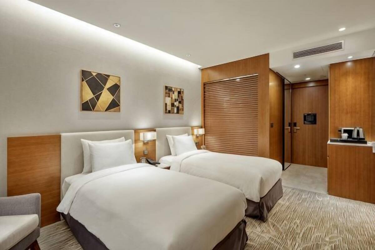 Une chambre d’hôtel avec deux lits, un bureau, une chaise et des œuvres d’art accrochées aux murs.