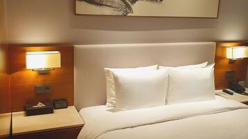 A hotel room with a large bed, two bedside lamps, a nightstand with a telephone, and a painting on the wall.