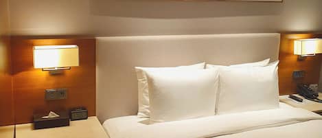 A hotel room with a large bed, two bedside lamps, a nightstand with a telephone, and a painting on the wall.