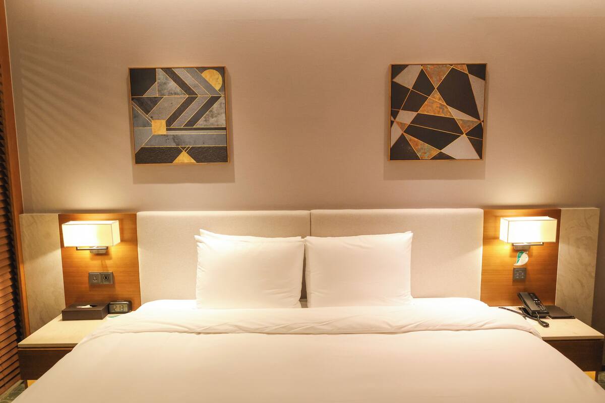 Une chambre d’hôtel avec un grand lit, deux tables de chevet avec des lampes, une horloge et des œuvres d’art abstraites accrochées au mur.