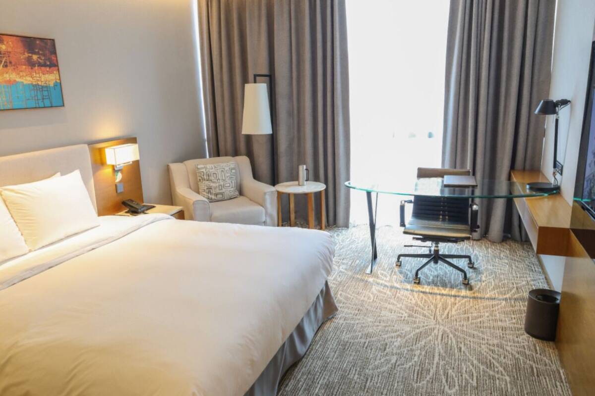 Une chambre d’hôtel avec un grand lit, un bureau, une chaise, une petite table et une lampe.