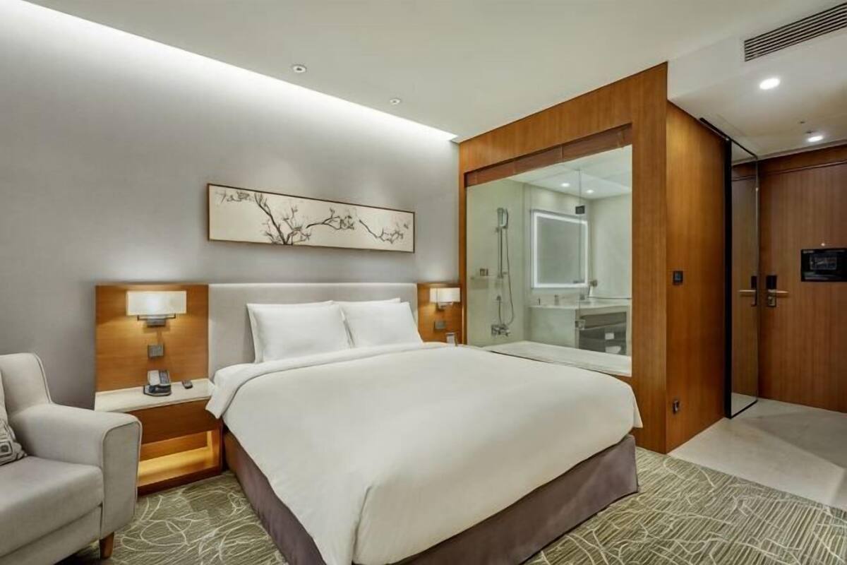 Une chambre d’hôtel avec un grand lit, deux tables de chevet avec des lampes, une armoire en bois, un grand miroir et une œuvre d’art accrochée au mur.