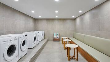 A laundry room with multiple washing machines, a bench, and small tables.
