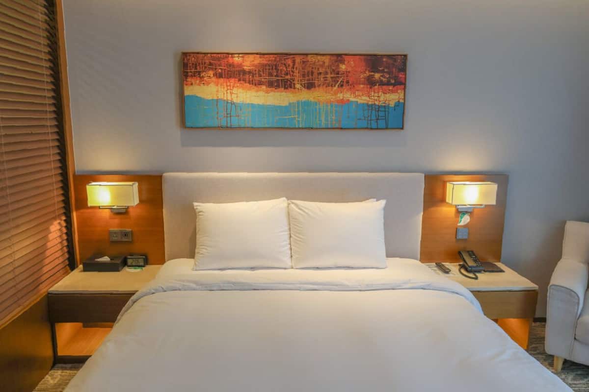 Une chambre d’hôtel avec un grand lit, deux tables de chevet avec des lampes, un tableau au mur et une chaise.