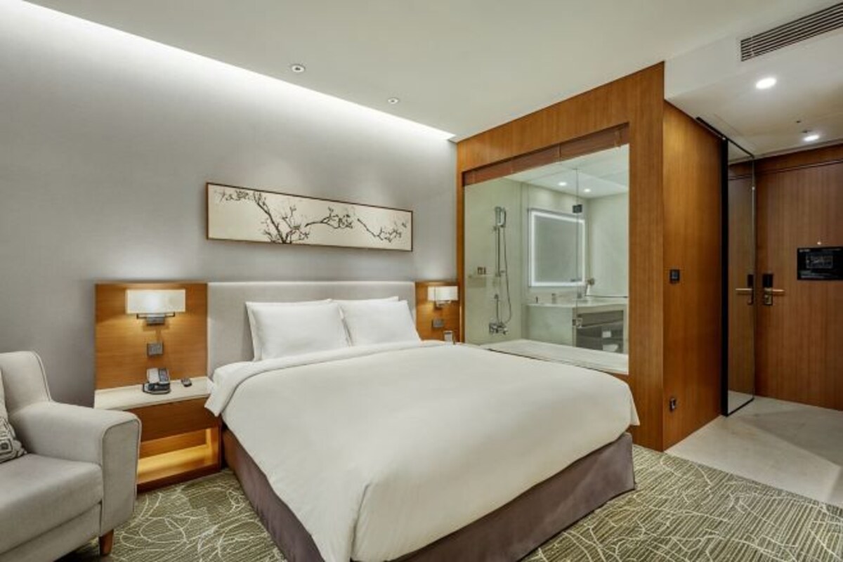 Une chambre d’hôtel avec un grand lit, deux tables de chevet avec des lampes, une armoire en bois, un grand miroir et une œuvre d’art accrochée au mur.
