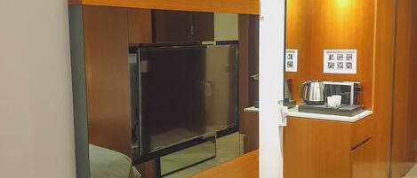 Una habitación de hotel con un armario de madera, una kitchenette pequeña y un televisor.