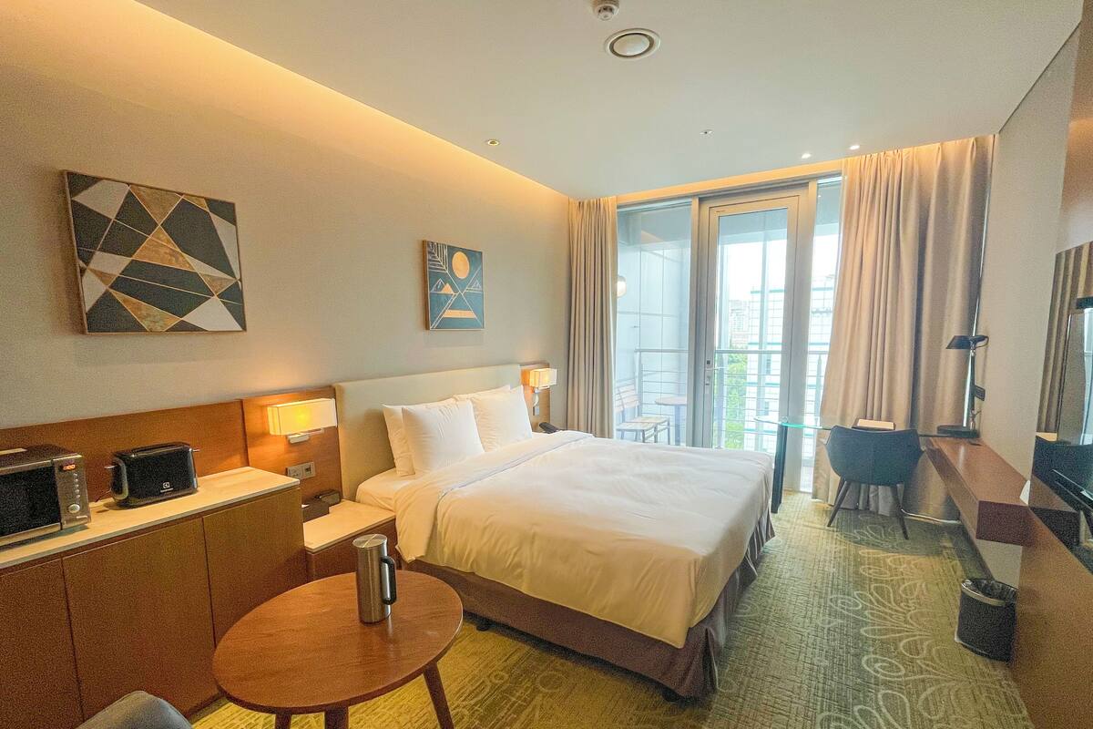 Une chambre d’hôtel comprenant un lit, un bureau avec un micro-ondes, une machine à café, une chaise et une vue sur l’extérieur.