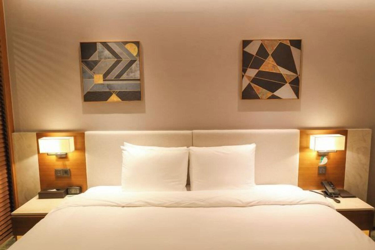 A hotel room with a large bed, two bedside tables with lamps, and abstract artwork on the walls.