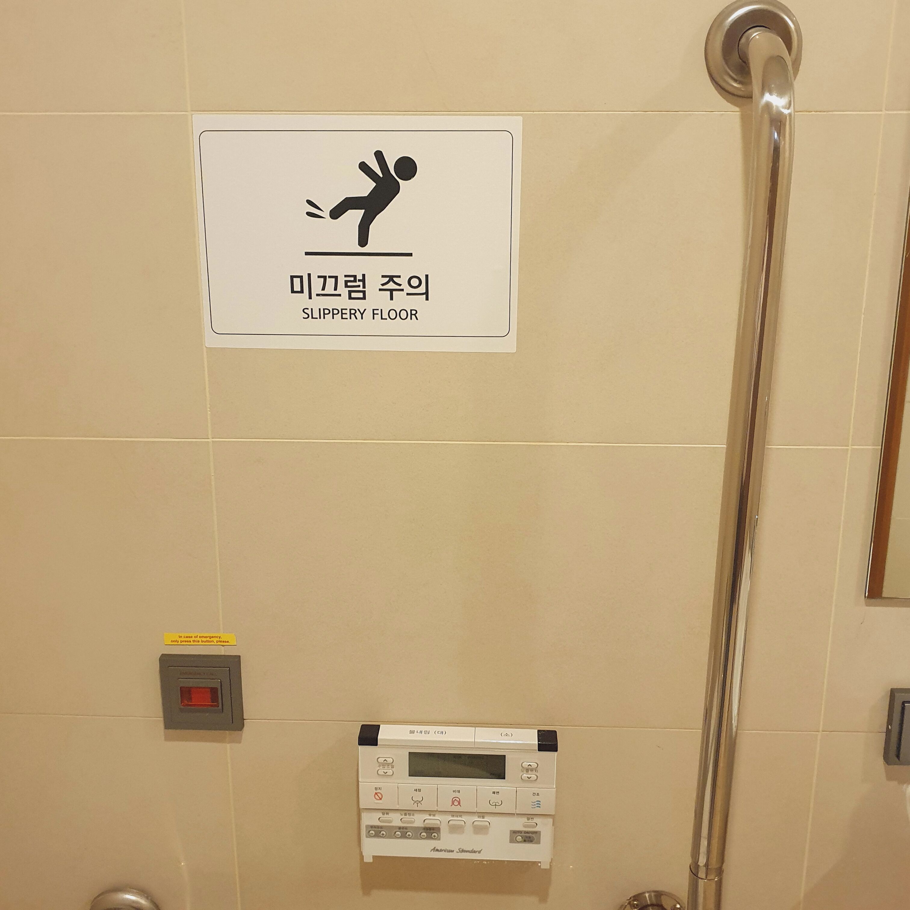 A sign indicating a slippery floor, a hand dryer, and a control panel for the shower.