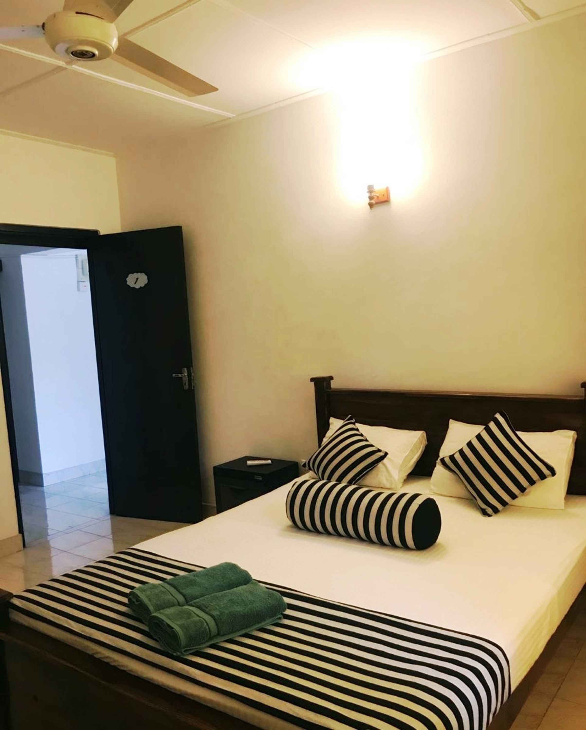 A hotel room with a bed, a nightstand, a desk, a ceiling fan, and a door.