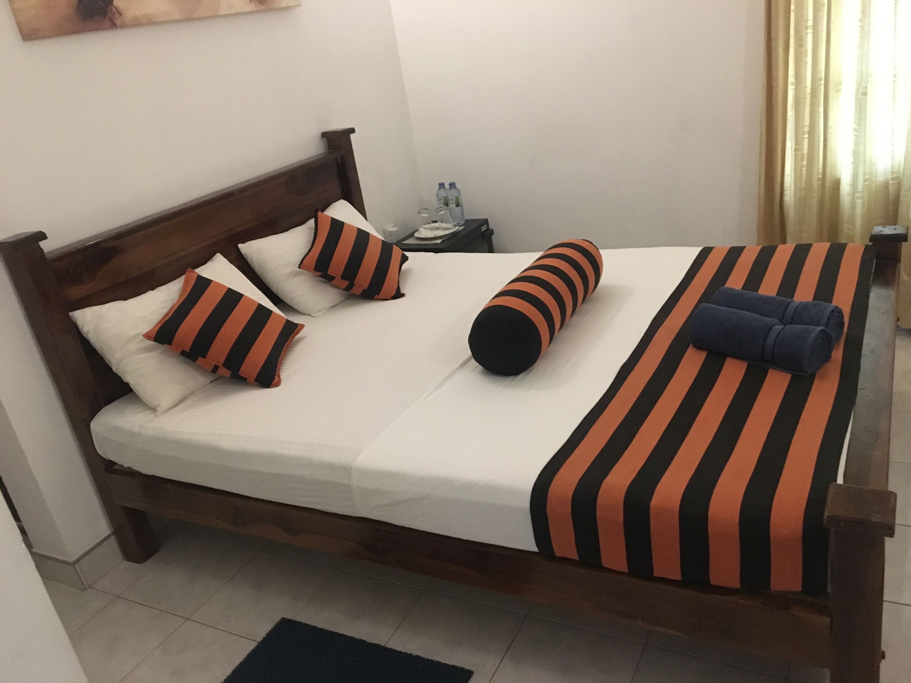 A neatly made bed with striped bedding and pillows, a wooden headboard, and a nightstand with a water bottle.
