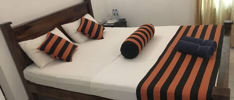 A neatly made bed with striped bedding and pillows, a wooden headboard, and a nightstand with a water bottle.