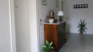 A hallway with a wooden dresser, a mirror, a vase with flowers, a lamp, and a potted plant.