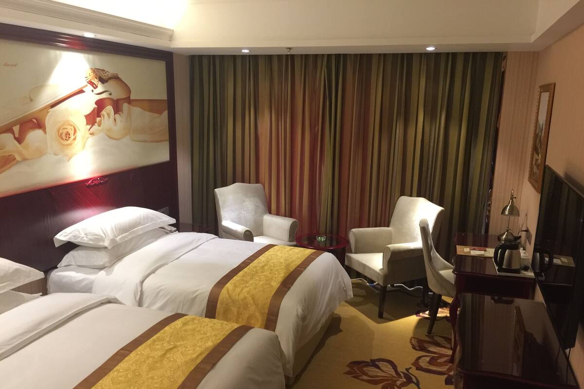 A hotel room with two beds, a desk, a chair, and a TV.
