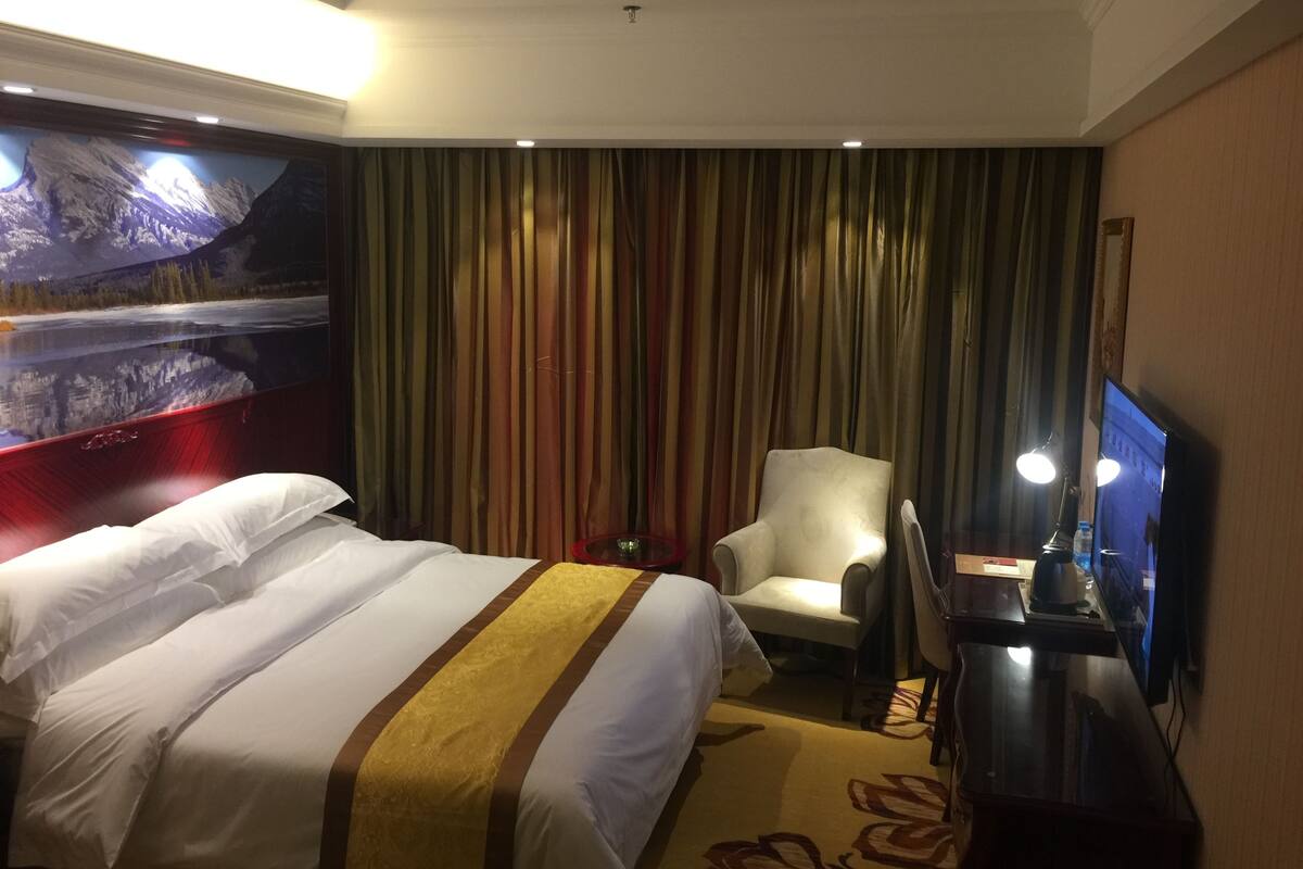 A hotel room with a bed, a chair, a desk, a television, and a large window with curtains.
