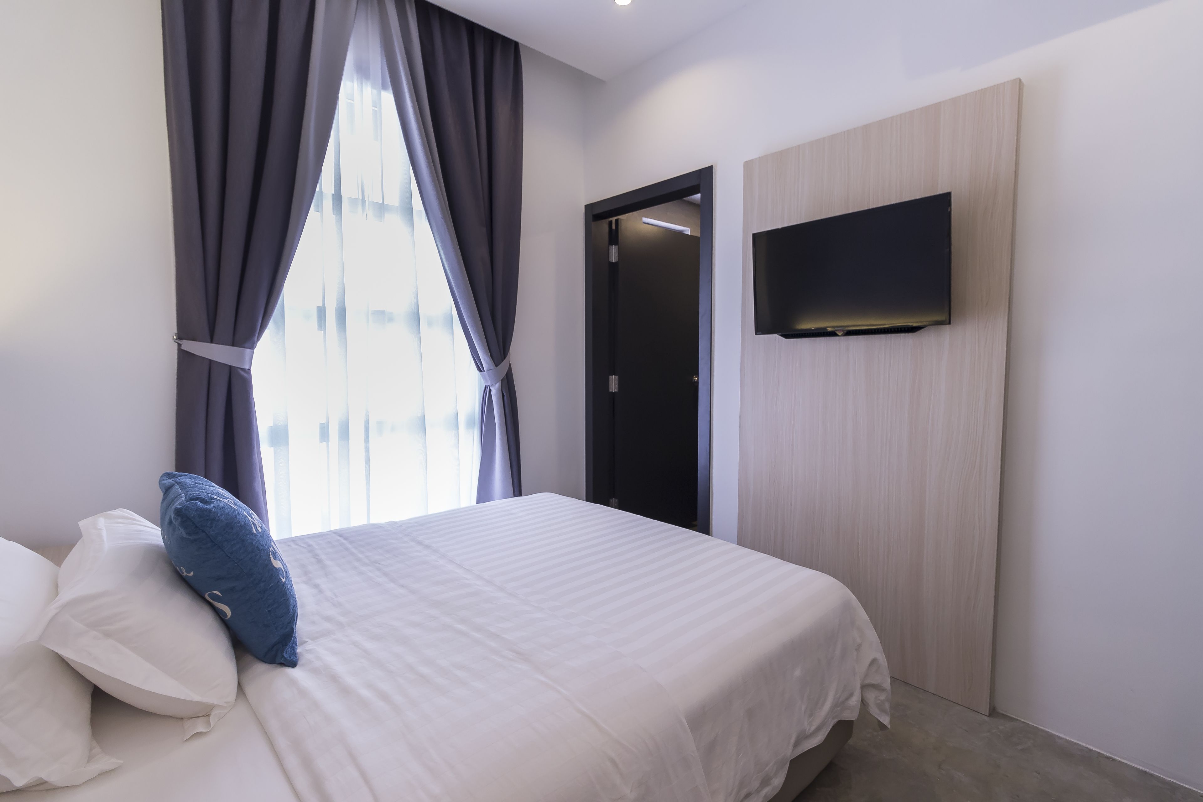 A modern hotel room with a large bed, a flat-screen TV mounted on the wall, and a view of the city through the window.