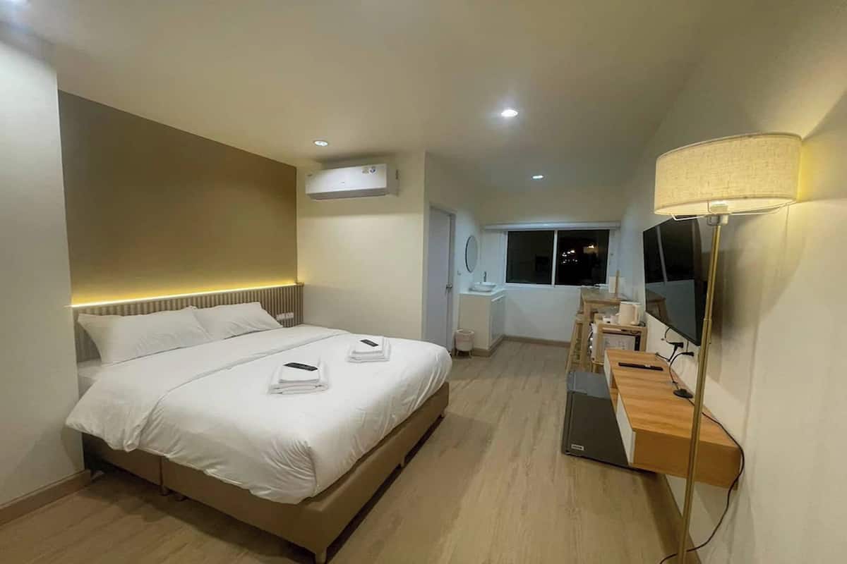 Quarto de hotel com cama, mesa de cabeceira, luminária, televisão e ar condicionado.