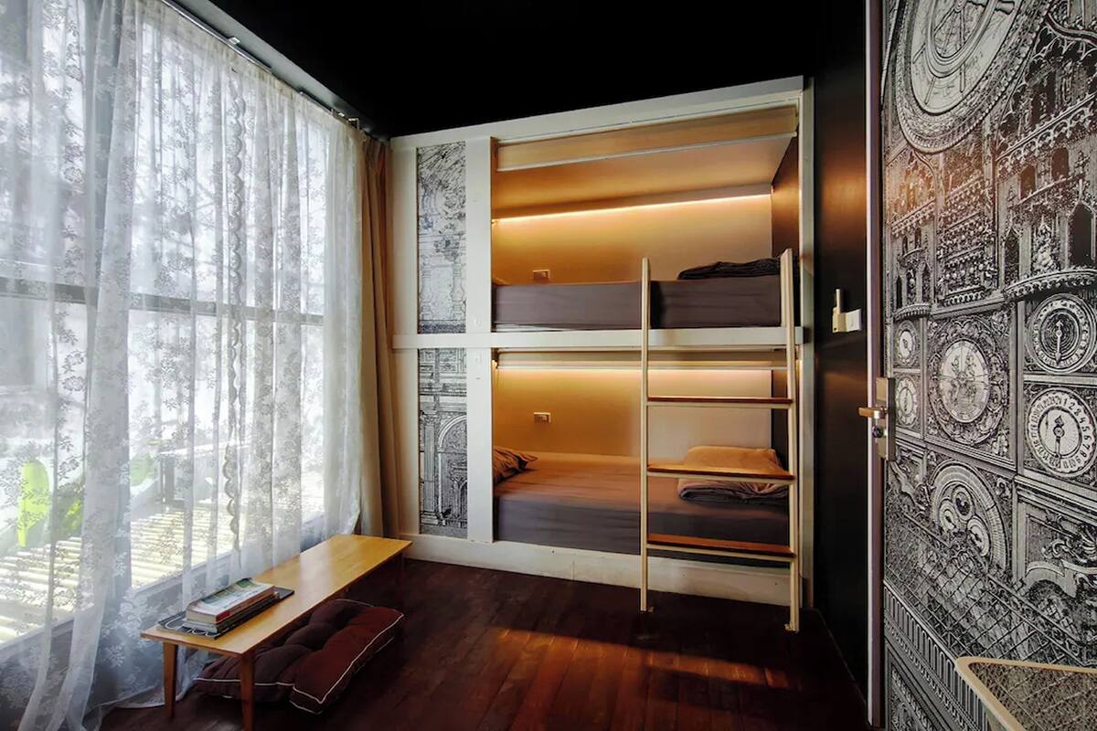 Quarto com uma janela grande, uma cama com cabeceira, uma mesa de cabeceira e uma parede com um mural detalhado.