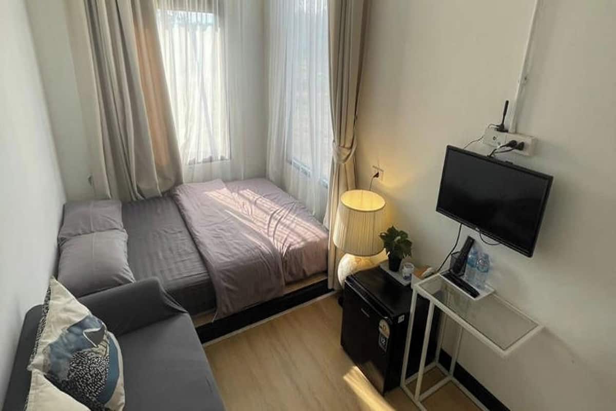 Um quarto com uma cama, uma televisão, uma escrivaninha e uma luminária.