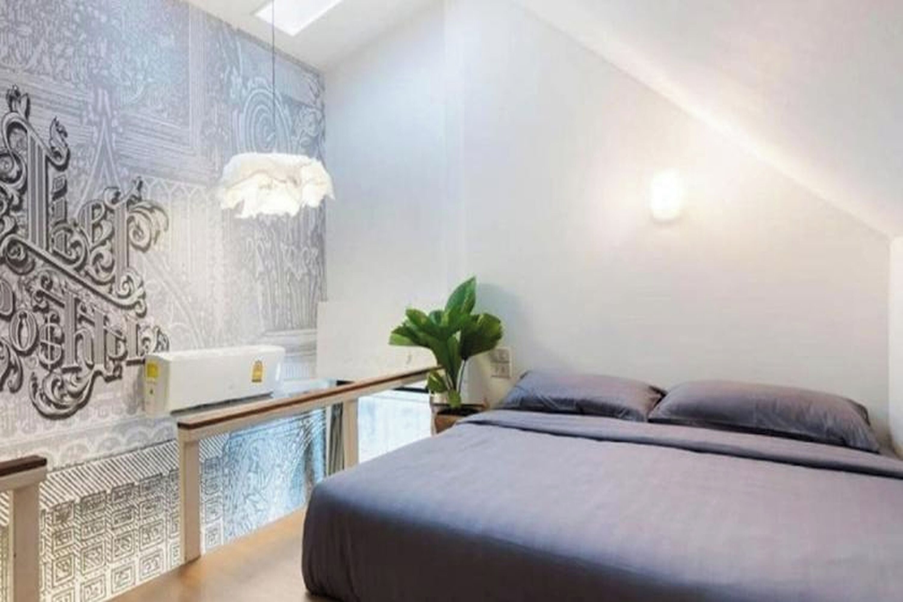 A bedroom with a bed, a nightstand, a plant, and a decorative wall.