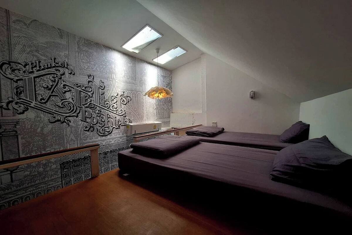 Quarto com duas camas, parede estampada e claraboia.