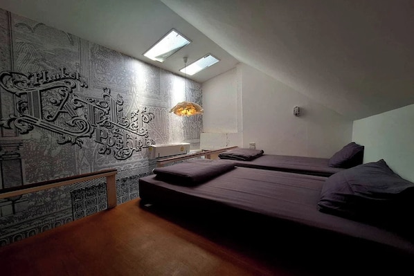 A bedroom with two beds, a patterned wall, and a skylight.
