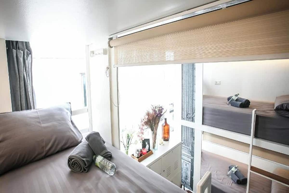 Quarto com cama, janela com vista, pequena mesa com objetos e beliche.