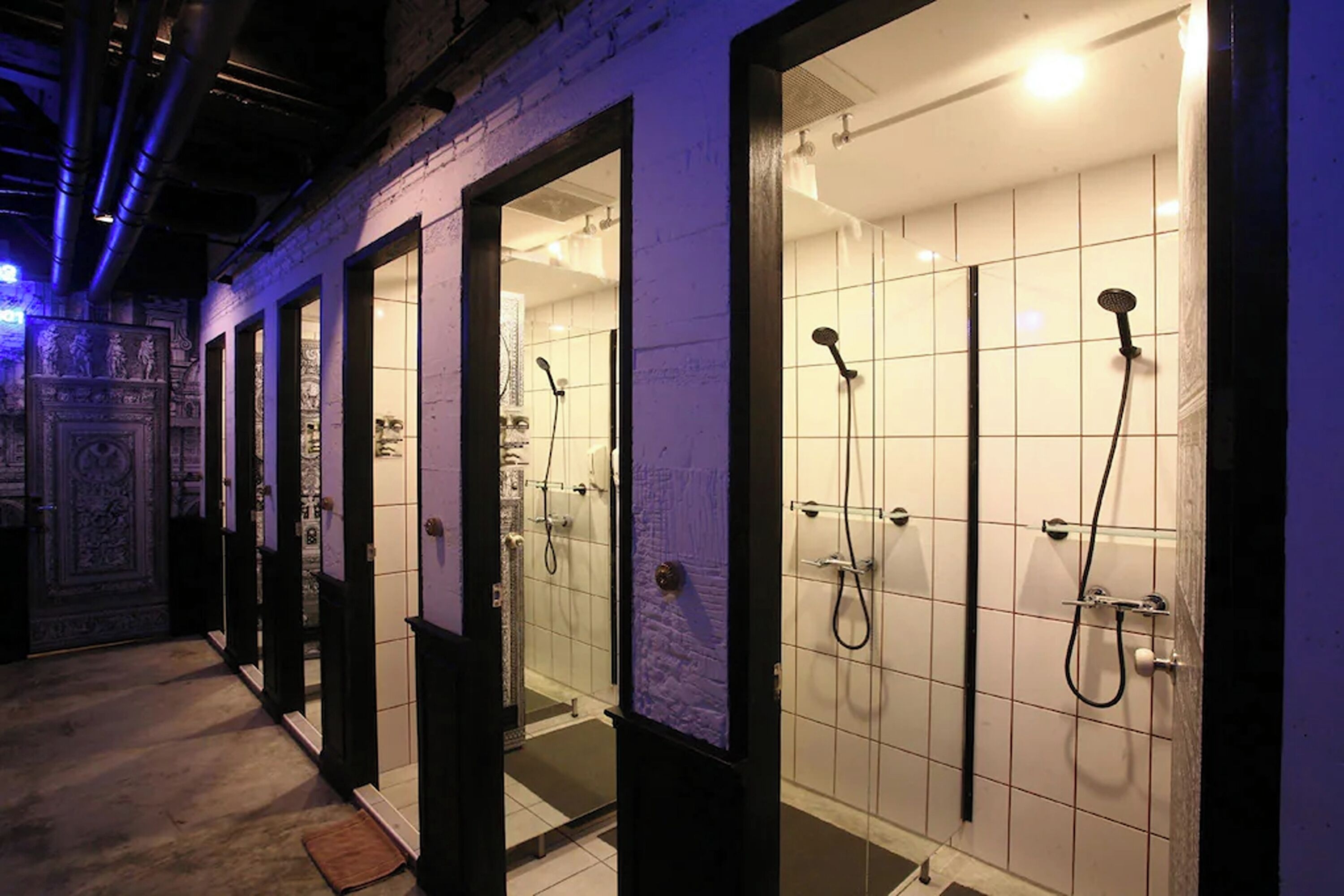 A row of glass-enclosed shower rooms with individual shower heads and a tiled floor.