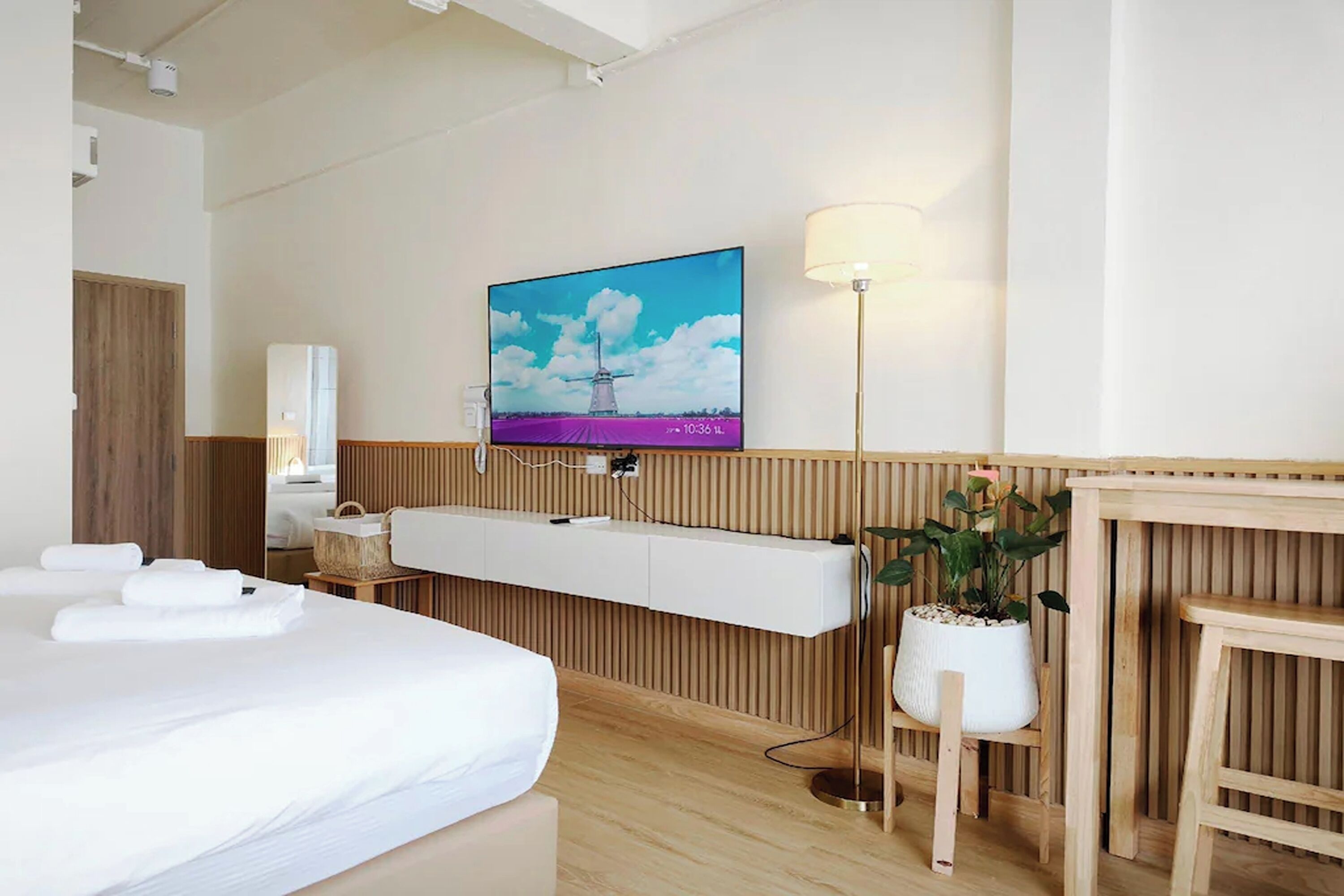 Une chambre d’hôtel avec un lit, un téléviseur fixé au mur, une table de chevet, une lampe et une plante en pot.