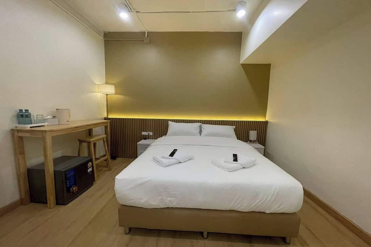 Quarto de hotel com cama, mesas de cabeceira, escrivaninha e luminária.