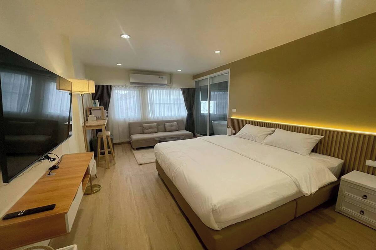 Quarto de hotel moderno com uma cama grande, televisão, escrivaninha, sofá e porta de vidro deslizante.