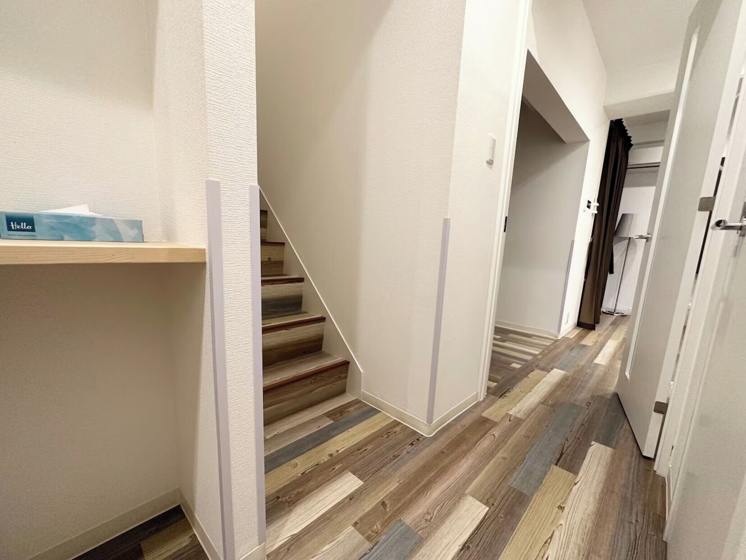 Un couloir avec un escalier en bois, une porte blanche et une étagère sur laquelle se trouve une boîte.
