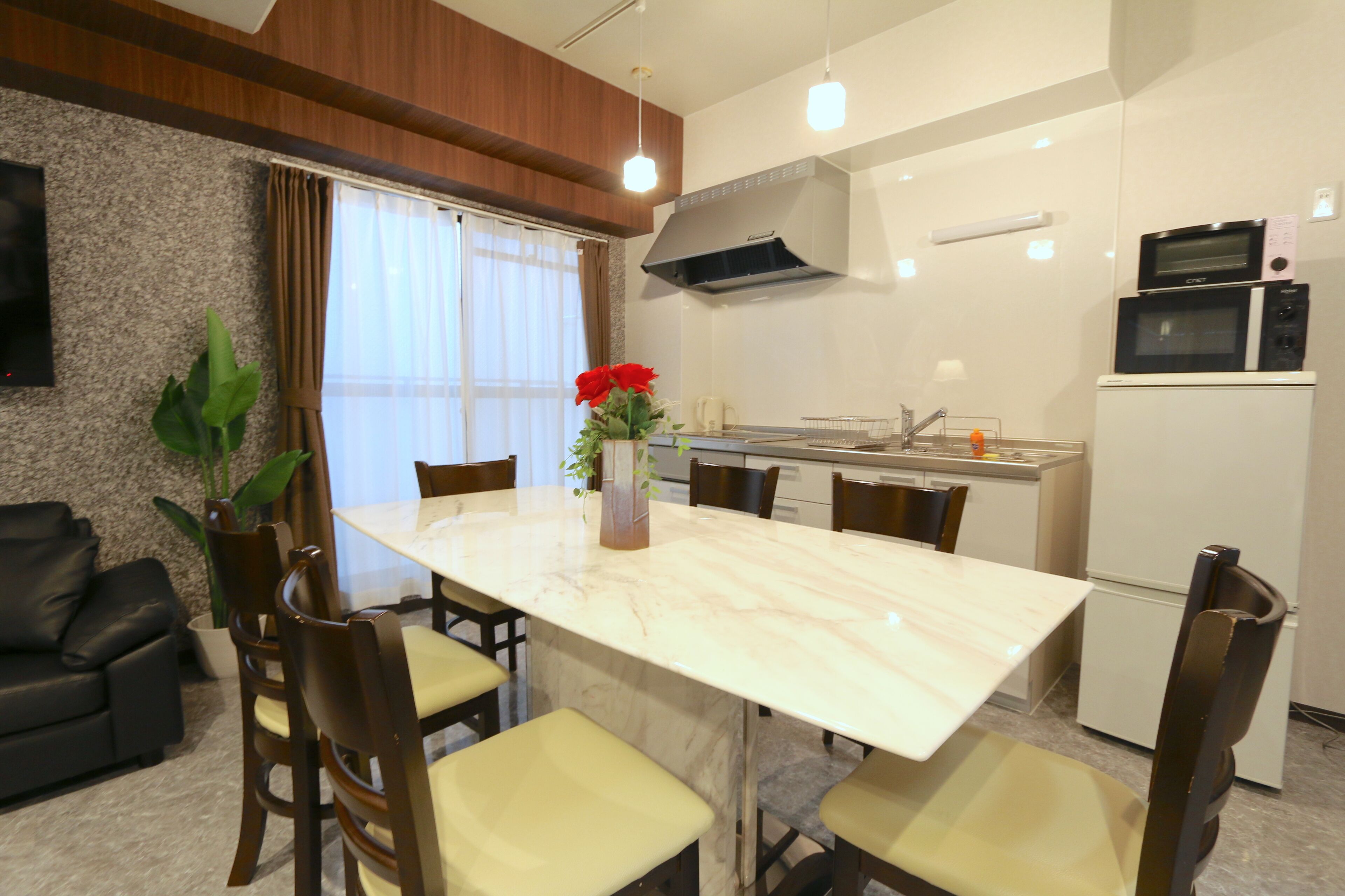 A modern kitchen with a marble countertop, a dining area with chairs, a black sofa, and a potted plant.