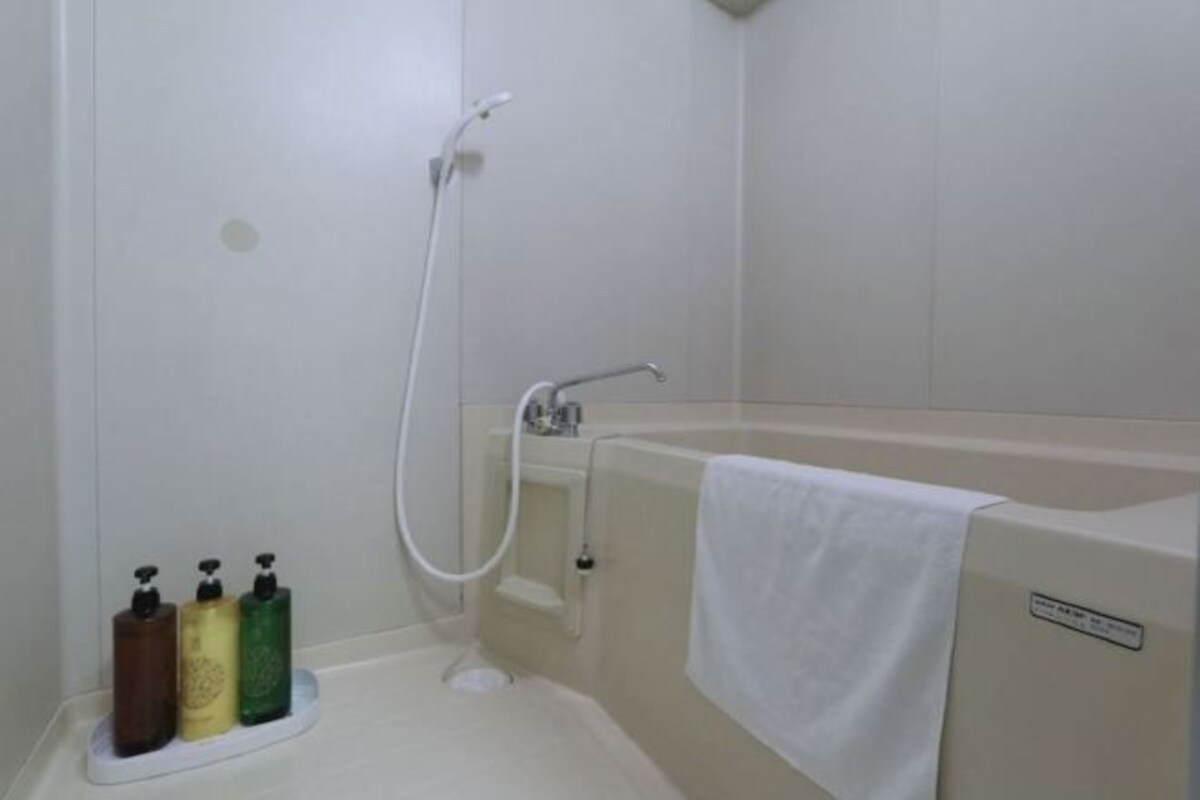 Un baño con bañera, ducha y tres botellas de jabón en un estante.