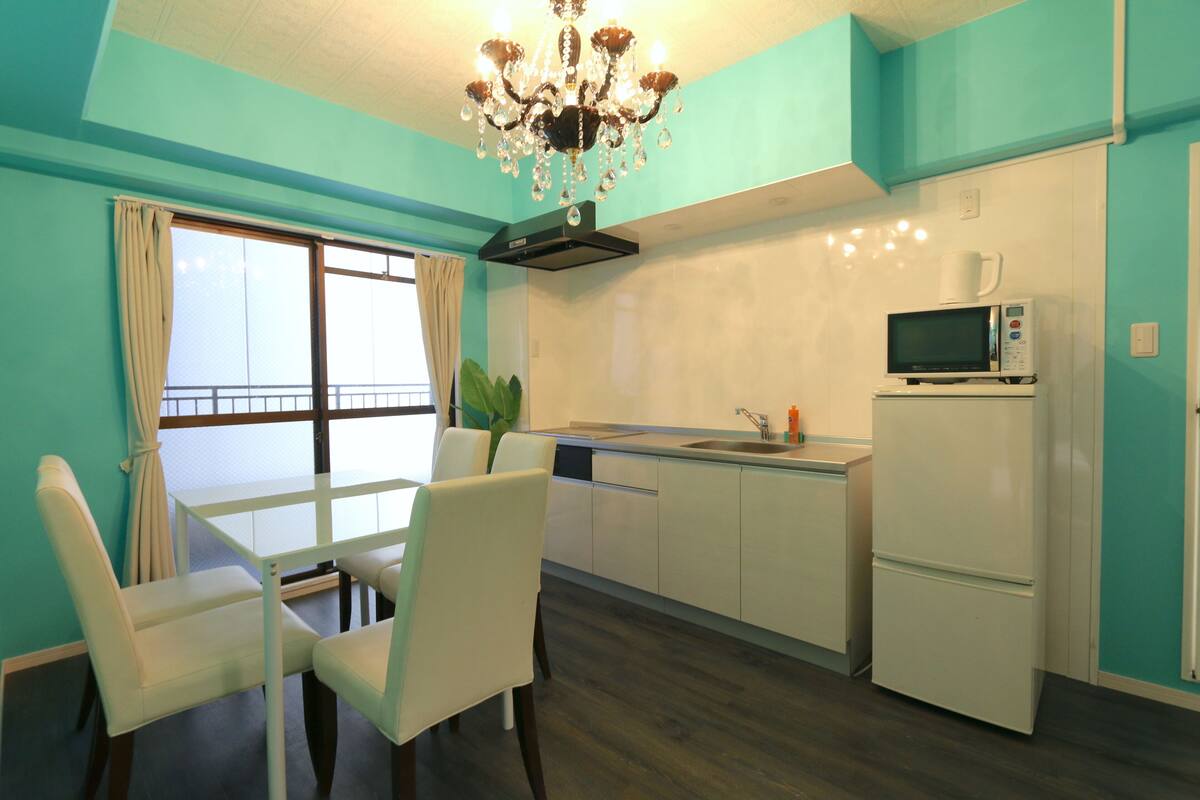 A compact kitchen with a dining area, a microwave, a refrigerator, and a chandelier.