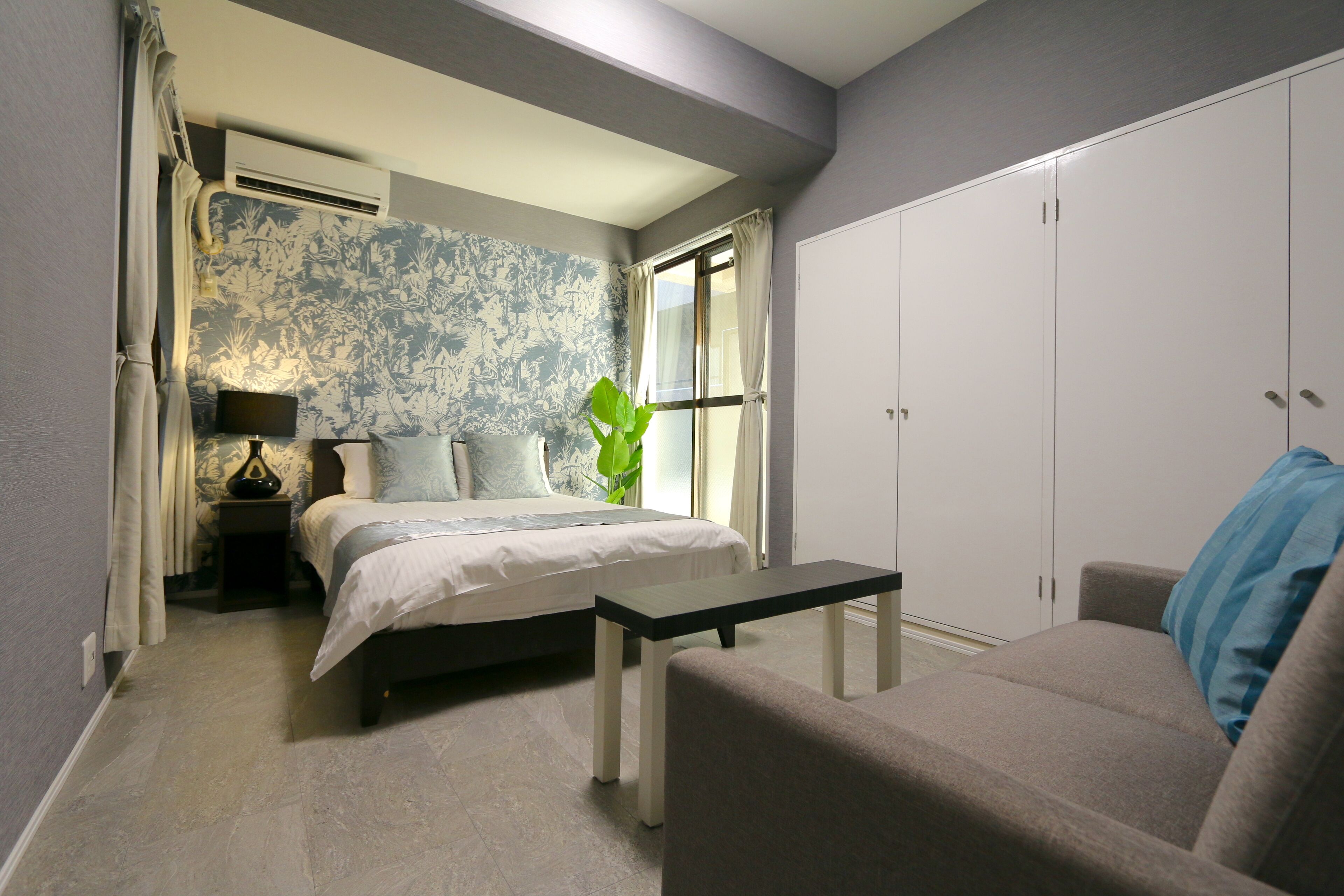 A bedroom with a bed, bedside table, lamp, and a window with curtains.
